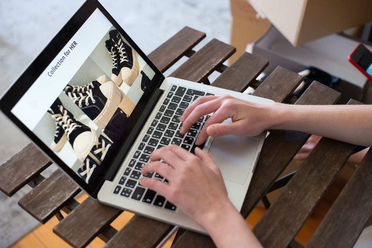 A person’s hands are browsing the HER collection on an online shoe shop with a laptop.